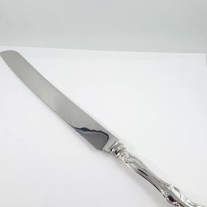 May include: A silver cake knife with a serrated blade and an ornate handle.