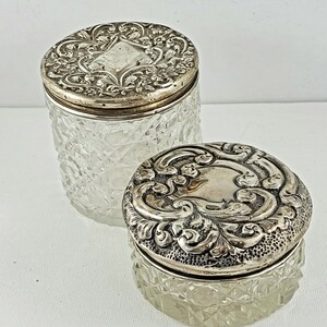 May include: Two clear glass jars with silver lids. The lids have an ornate floral design.