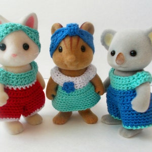 May include: Three crocheted outfits for small stuffed animals. The outfits are in shades of blue, red, and white. The outfits are designed for a cat, a squirrel, and a koala.