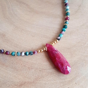 Op de afbeelding: Een delicate ketting met een traanvormige robijn hanger. De ketting is gemaakt met kleine, veelkleurige kralen en gouden accenten.