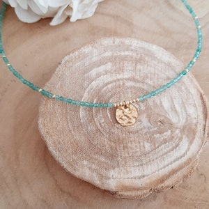 K&ouml;nnte beinhalten: Eine zarte Halskette aus gr&uuml;nen Edelsteinen mit einem goldenen Anh&auml;nger. Der Anh&auml;nger ist ein geh&auml;mmerter Kreis mit einer strukturierten Oberfl&auml;che.