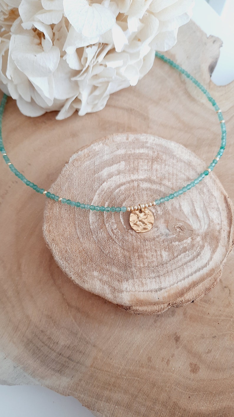 K&ouml;nnte beinhalten: Eine zarte Halskette aus gr&uuml;nen Edelsteinen mit einem goldenen Anh&auml;nger. Der Anh&auml;nger ist ein geh&auml;mmerter Kreis mit einer strukturierten Oberfl&auml;che.