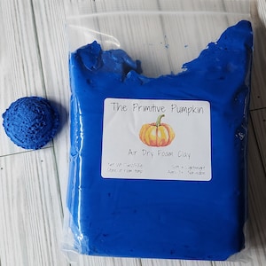 May include: A package of bright blue air dry foam clay from "The Primitive Pumpkin" with a pumpkin graphic. The package is next to a small, round, blue foam clay shape. The package is labeled as 17oz/500g, soft, lightweight, and non-edible.