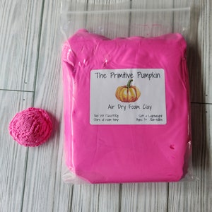 May include: A package of bright pink air dry foam clay from "The Primitive Pumpkin" with a small, textured ball of the same clay. The package label includes a pumpkin illustration and the text "Air Dry Foam Clay".