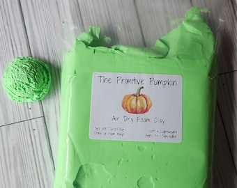 Puede incluir: Un paquete de arcilla de espuma de secado al aire de color verde brillante de "The Primitive Pumpkin" con una bola de la misma arcilla al lado. La etiqueta dice "Peso neto 500g, Suave + Ligero, A partir de 3 años No comestible."
