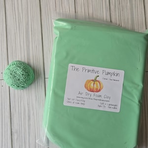 May include: A rectangular package of light green air dry foam clay with a label reading The Primitive Pumpkin, Air Dry Foam Clay, Net Wt 17.6oz/500g, Soft, Lightweight, Ages 3+, Non-edible, and a small textured green foam ball beside it.