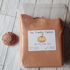 May include: A package of air dry foam clay in a clear plastic bag, with a small, textured ball of clay to the left. The label reads "The Primitive Pumpkin" with a pumpkin illustration. The net weight is 16oz/500g.