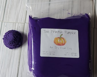 Puede incluir: Una bolsa morada de arcilla de espuma de secado al aire con una etiqueta que dice "The Primitive Pumpkin Air Dry Foam Clay" con una ilustración de calabaza. La etiqueta también dice "Net Wt 17.6oz/500g Store at room temp Soft + Lightweight Ages 3+ Non-edible".