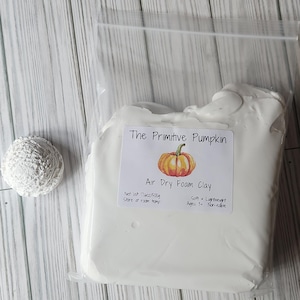 May include: A package of white air dry foam clay with a label that reads "The Primitive Pumpkin" and features a pumpkin illustration. A small, textured, white ball is to the left of the package. The package weighs 17.6oz/500g.