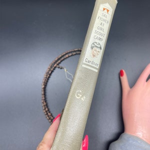 May include: A vintage paperback book titled "Sal Fisher at Girl Scout Camp" by Gardner. The cover features a black and white illustration of a young girl with short hair.