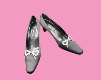 May include: A pair of black satin pumps with a rhinestone bow detail. The shoes are labeled "Vanelj".
