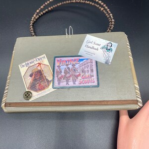 May include: A green fabric purse with a wooden beaded handle. The purse has a vintage Girl Scout patch, a "The Literary Digest" magazine cover, and a Girl Scout Handbook.
