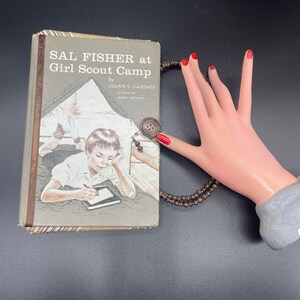 May include: A vintage book titled "Sal Fisher at Girl Scout Camp" by Lillian S. Gardner with illustrations by Mary Stevens. The book cover features a drawing of a girl sitting in a tent, writing in a notebook.