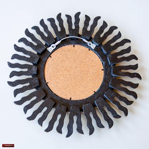 May include: Black sunburst mirror with a round, cork-backed mirror. The mirror has a wire hanger on the back.