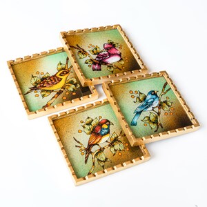 May include: Set of four square coasters with gold trim. Each coaster features a different bird painted on a green background with gold accents. The birds are a yellow bird, a blue bird, a red and yellow bird, and a pink bird.
