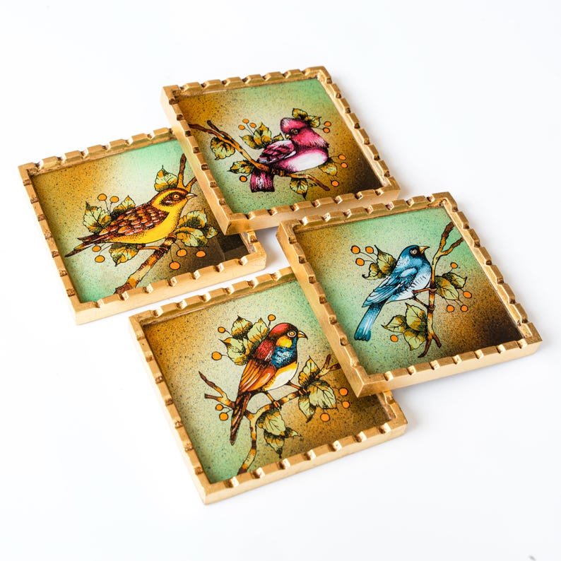 May include: Set of four square coasters with gold trim. Each coaster features a different bird painted on a green background with gold accents. The birds are a yellow bird, a blue bird, a red and yellow bird, and a pink bird.