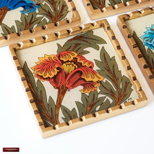 May include: Set of four coasters with a gold frame and a floral design. Each coaster features a different colored flower with a yellow center. The flowers are surrounded by green leaves.