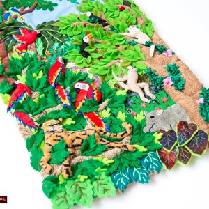 May include: A colorful felt wall hanging depicting a jungle scene with a tiger, monkeys, toucans, parrots, and other animals. The hanging is made of felt and has a textured background.