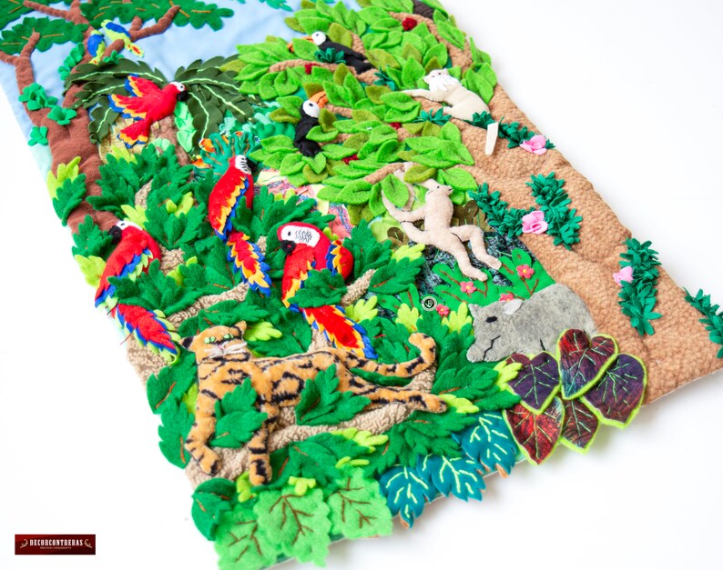 May include: A colorful felt wall hanging depicting a jungle scene with a tiger, monkeys, toucans, parrots, and other animals. The hanging is made of felt and has a textured background.
