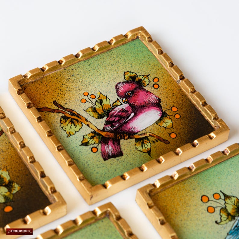 May include: Set of four square coasters with a gold frame. Each coaster features a different painted bird on a branch with green leaves and orange berries. The birds are pink, blue, green, and yellow.