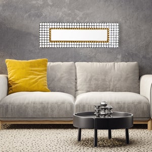 May include: A gray sofa with a yellow pillow sits in front of a gray wall with a rectangular mirror with a gold frame. A black coffee table with a silver sculpture sits in front of the sofa.