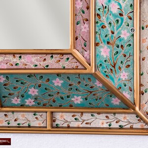 May include: A gold-toned mirror frame with a decorative design of pink flowers and green leaves on a turquoise background.