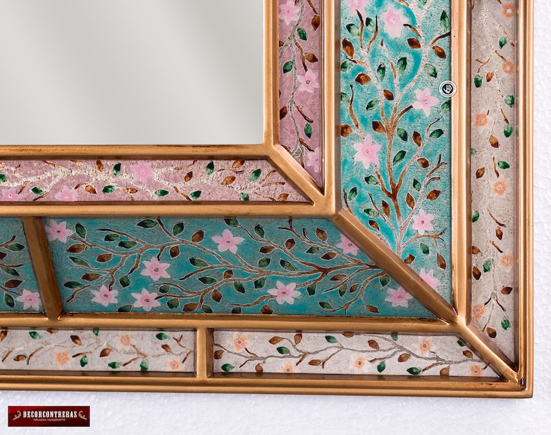May include: A gold-toned mirror frame with a decorative design of pink flowers and green leaves on a turquoise background.