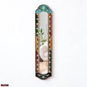 Puede incluir: Un espejo alto y estrecho con un marco decorativo. El marco está hecho de madera y está pintado en una variedad de colores, incluyendo negro, dorado, rojo, verde y azul. El marco está decorado con un patrón floral. El espejo está arqueado en la parte superior y tiene un borde biselado.