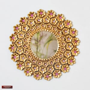 Peut inclure: Miroir rond décoratif avec un cadre doré. Le cadre est orné de nombreux ornements en forme de fleurs dorées, chacune avec un centre rose. La surface réfléchissante du miroir est circulaire.