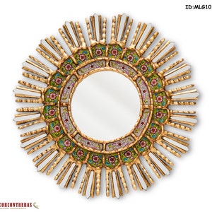 Round sunburst wall mirror of 17.7 inches seen straight on. Two rings of reverse painted glass circle the central mirror: a deep green band of pink and red flowers inside, a colonial ivory arc outside. Gilded carved rays radiate outward with slim mirrored pieces set between them.