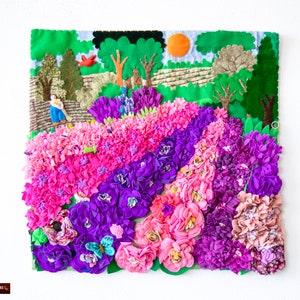 Può includere: Un arazzo da parete in tessuto colorato che rappresenta una scena da giardino con fiori rosa, viola e verdi. Lo sfondo presenta un cielo blu con un sole giallo e alberi verdi.