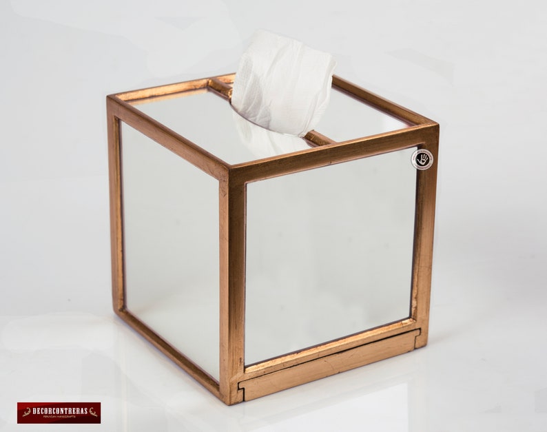 K&ouml;nnte beinhalten: Ein goldfarbener, spiegelnder Taschentuchhalter mit quadratischer Form und einer transparenten Glasoberfl&auml;che. Die Box hat einen goldenen Rand um die Kanten und ein kleines goldenes Etikett an der Seite.