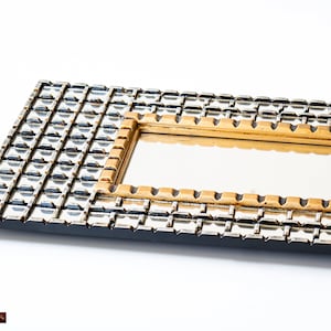 May include: A rectangular mirror with a black frame and a gold inner frame. The frame is decorated with a geometric pattern of small squares.