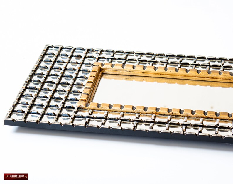 May include: A rectangular mirror with a black frame and a gold inner frame. The frame is decorated with a geometric pattern of small squares.