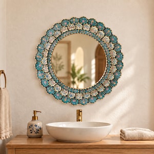 Round gold framed mirror hanging above a bathroom vanity, shown in a styled room to give a sense of its 23.6 inch scale against a standard sink. The hand painted turquoise floral glass and antique gold finish warm up white tile, brass fixtures and warm wood tones.