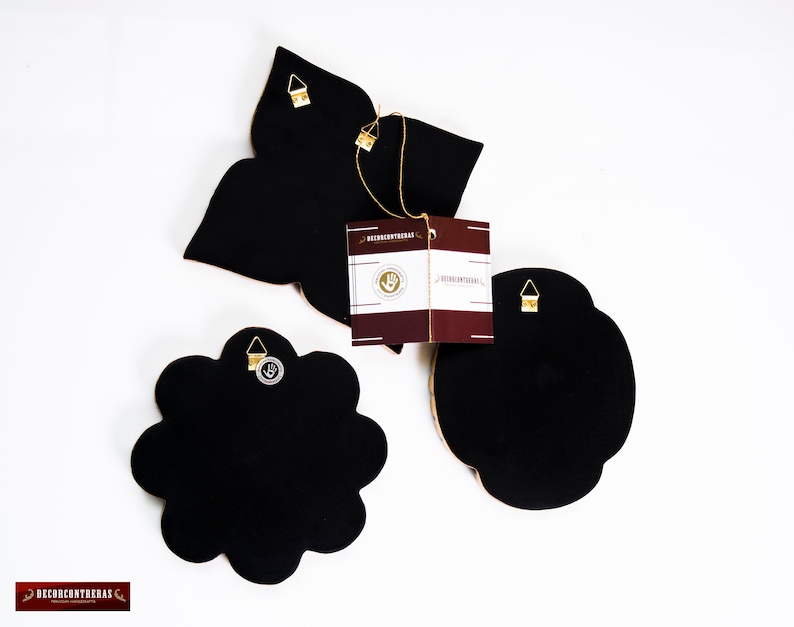 Puede incluir: Tres piezas de decoraci&oacute;n de pared negras con detalles dorados. Cada pieza tiene una forma diferente, incluyendo una flor, una estrella y una forma redondeada. Las piezas tienen un gancho para colgar en la parte posterior.