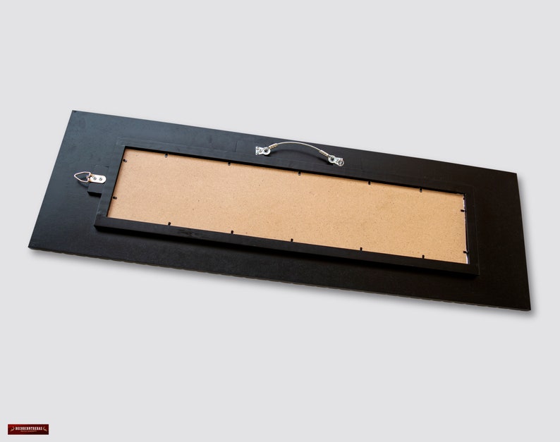 May include: The back of a black framed rectangular mirror with a brown cardboard backing. The mirror has a metal hanging wire and a hook for hanging.