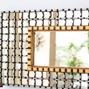 May include: A gold framed mirror with a grid pattern of smaller mirrors. The mirror is reflecting a plant and a blurry background.