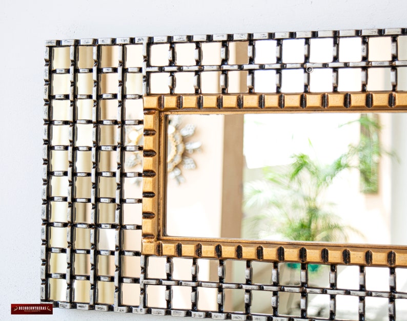 May include: A gold framed mirror with a grid pattern of smaller mirrors. The mirror is reflecting a plant and a blurry background.