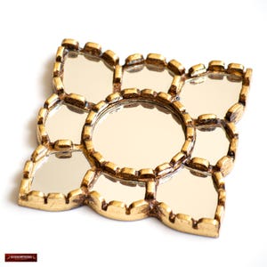 May include: A decorative gold-colored mirror with a unique floral design. The mirror features multiple small, reflective surfaces arranged around a central, larger mirror. The frame has an ornate, textured appearance, adding to its vintage aesthetic.
