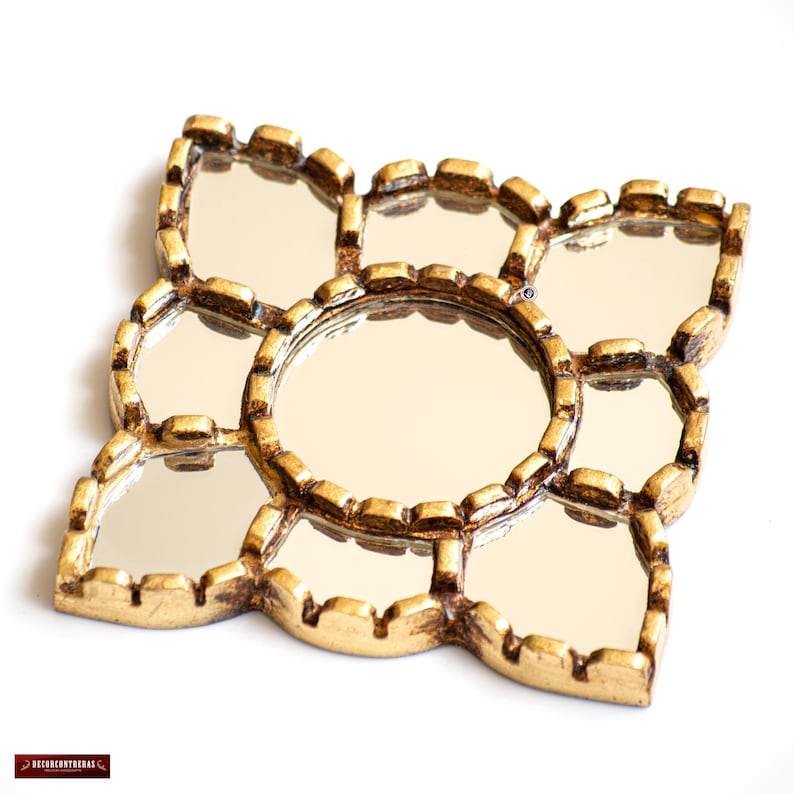 May include: A decorative gold-colored mirror with a unique floral design. The mirror features multiple small, reflective surfaces arranged around a central, larger mirror. The frame has an ornate, textured appearance, adding to its vintage aesthetic.
