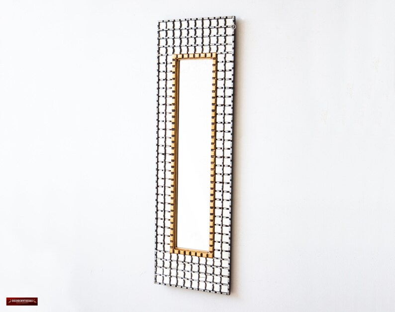 May include: A rectangular mirror with a black and white checkered frame and a gold border. The mirror is hanging on a white wall.
