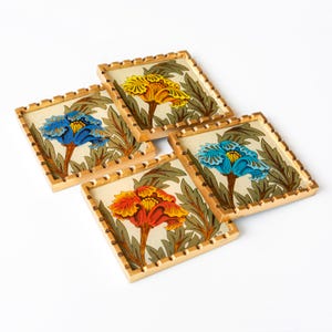 May include: Set of four square coasters with a gold trim and a floral design. Each coaster features a different colored flower: yellow, blue, orange, and red.