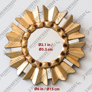 May include: A gold-coloured sunburst mirror with a central circular mirror. The frame features a textured, radiating design. The overall diameter is 15 cm, and the central mirror is 5.3 cm in diameter.