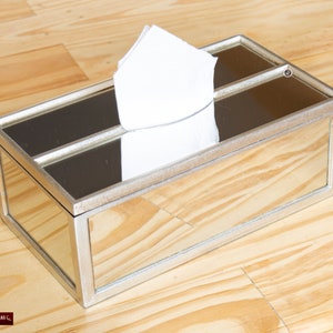 May include: Silver mirrored tissue box holder with a white tissue inside. The holder has a rectangular shape and a silver frame.
