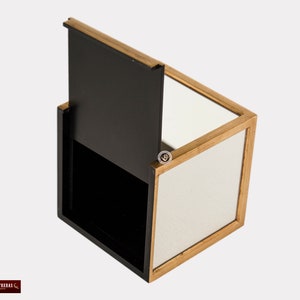 K&ouml;nnte beinhalten: Eine kleine, quadratische Holzkiste mit einem Scharnierdeckel. Die Kiste ist aus dunklem Holz mit goldener Verzierung. Das Innere der Kiste ist mit einem Spiegel ausgekleidet.