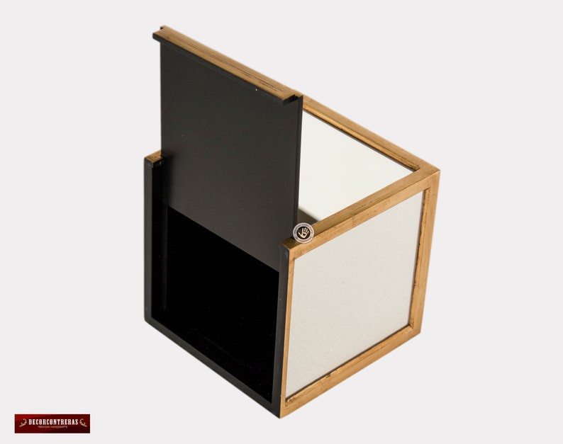 K&ouml;nnte beinhalten: Eine kleine, quadratische Holzkiste mit einem Scharnierdeckel. Die Kiste ist aus dunklem Holz mit goldener Verzierung. Das Innere der Kiste ist mit einem Spiegel ausgekleidet.