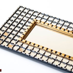 May include: A rectangular mirror with a gold and silver grid pattern frame. The frame is made of small squares that are arranged in a grid pattern. The mirror is surrounded by a gold frame.
