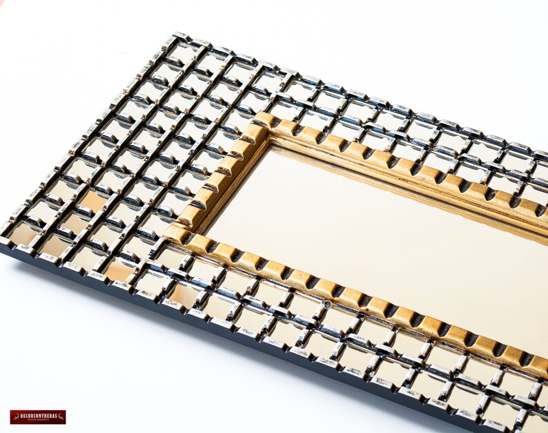 May include: A rectangular mirror with a gold and silver grid pattern frame. The frame is made of small squares that are arranged in a grid pattern. The mirror is surrounded by a gold frame.
