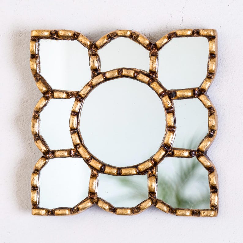 May include: A decorative wall mirror with a gold-colored frame. The mirror has a central circular mirror surrounded by eight smaller mirrors in a geometric pattern. The frame has a textured, ornate design.